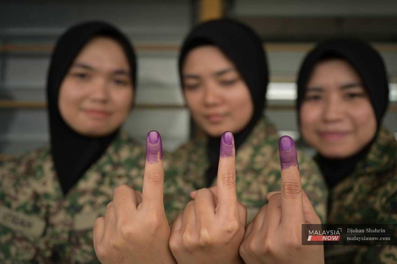 Army personnel hold up their ink-stained fingers after casting their ballot papers at the Sungai Besi camp. 