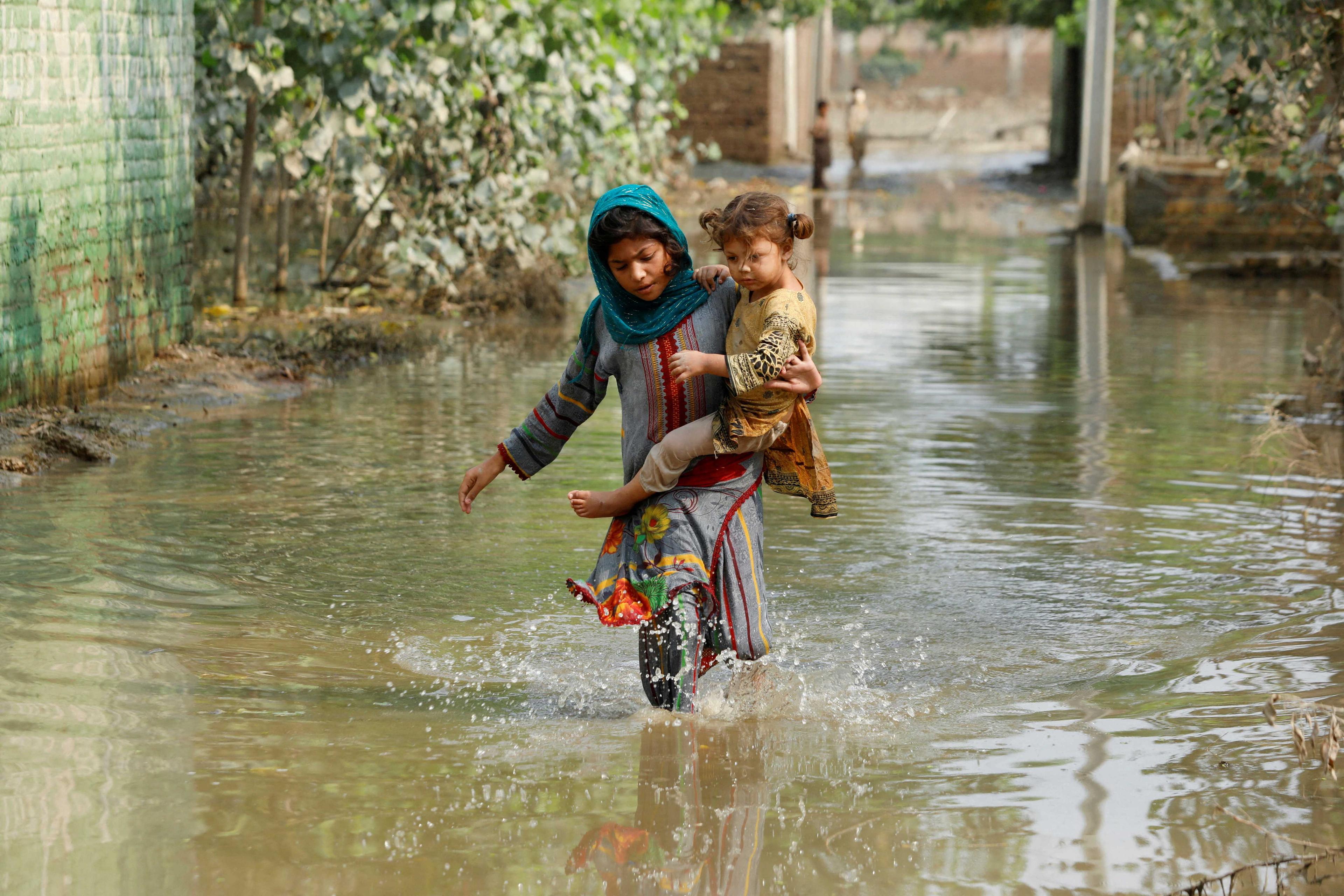 A girl carries her sibling as she walks through stranded flood water, following rains and floods during the monsoon season in Nowshera, Pakistan Sept 4. Photo: Reuters