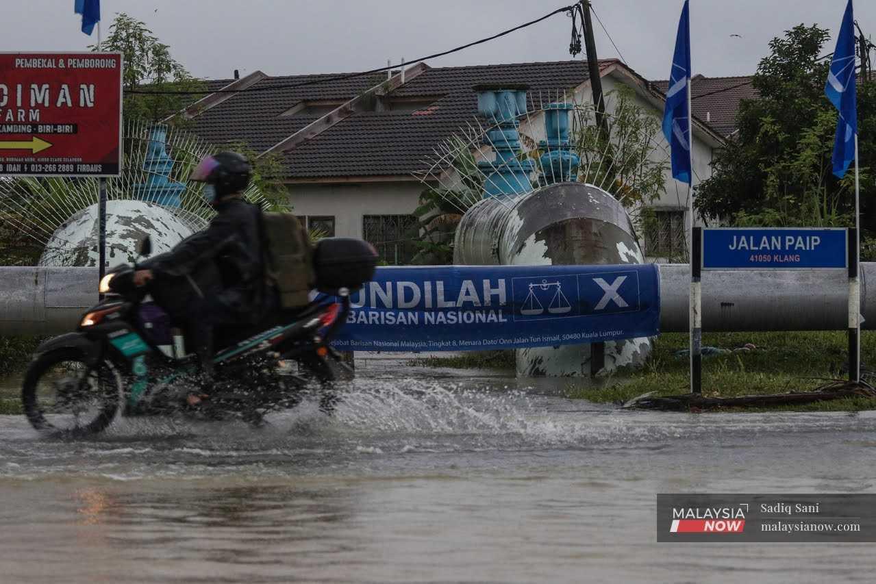 Seorang penunggang motorsikal meredah banjir di Jalan Paip, Meru Klang melewati bendera Barisan Nasional. 