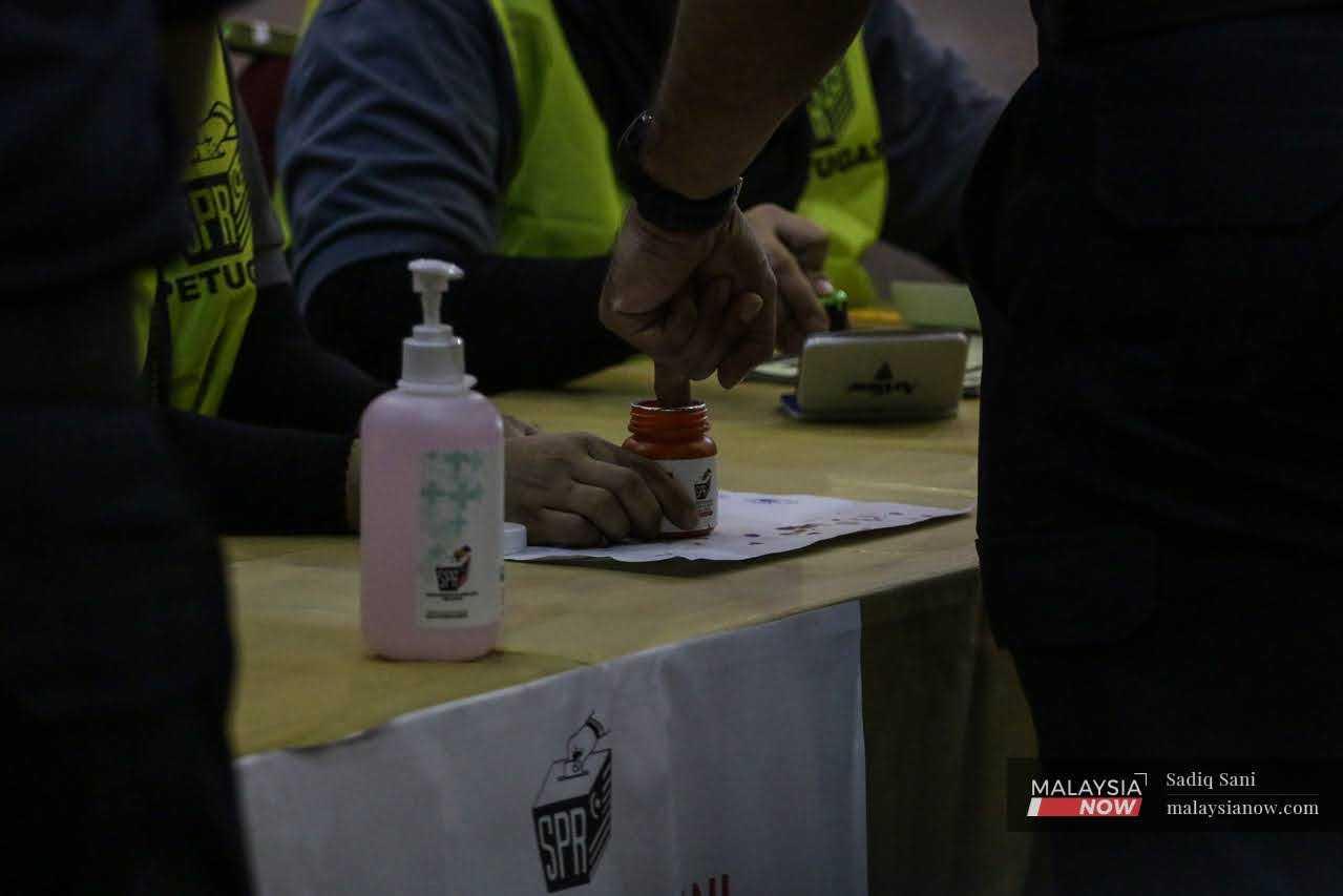 Anggota polis mencelup jari dalam bekas dakwat selepas membuang undi pada hari pengundian awal semalam.