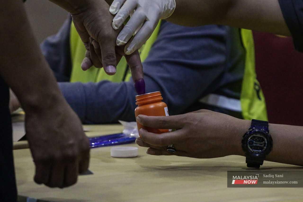 A police officer dips his finger into a jar of permanent ink during early voting in Shah Alam on Nov 15. 