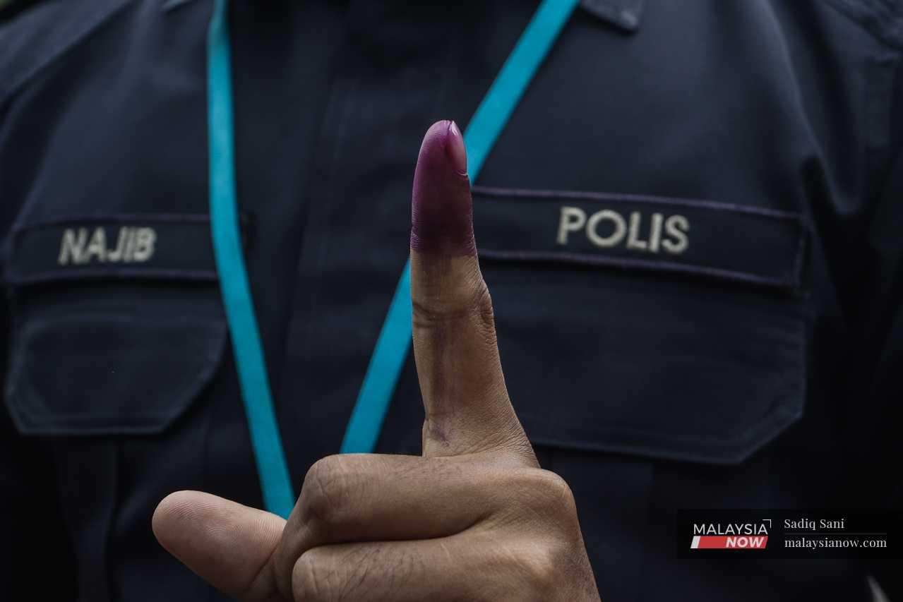 A police officer holds up his ink-stained finger after casting his vote. 