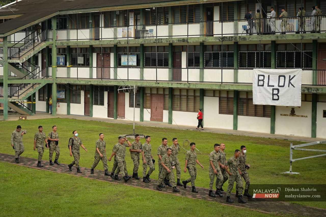 Servicemen in their military uniforms cross a field at the Sungai Besi army camp.