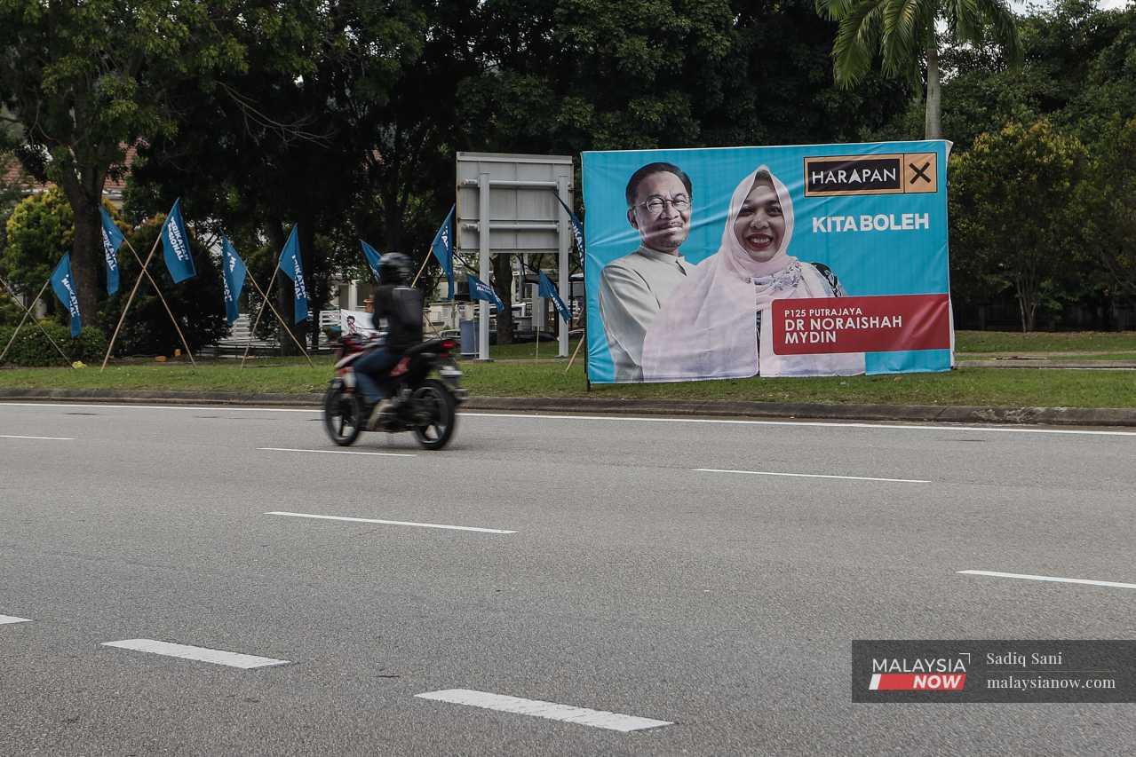 A motorcyclist passes a billboard featuring Pakatan Harapan's candidate, Noraishah Mydin Abdul Aziz, alongside the coalition's chairman, Anwar Ibrahim.