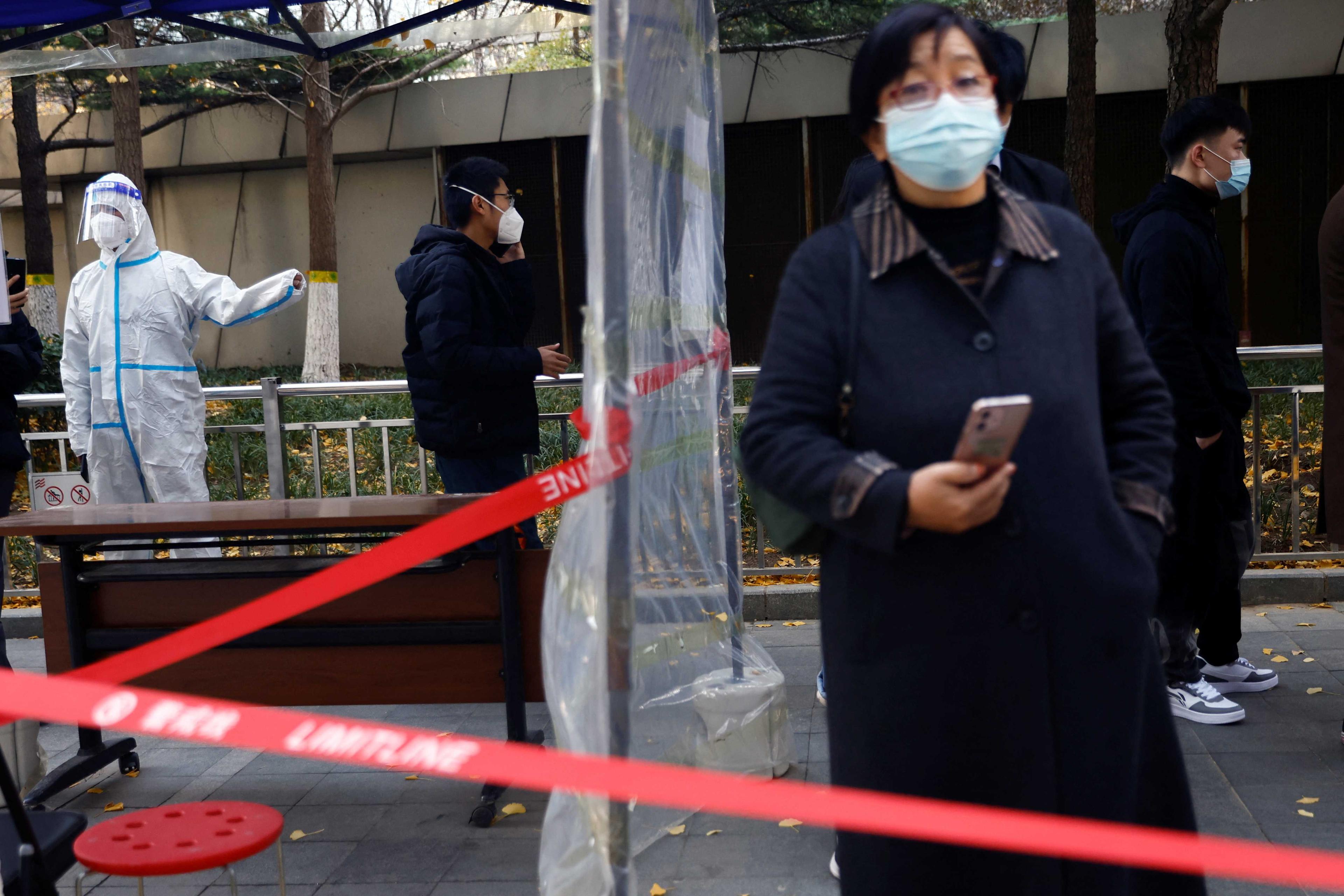A worker in a protective suit guides people to take a nucleic acid test for Covid-19 at a testing booth near an office building in Central Business District in Chaoyang district, Beijing, China on Nov 15. Photo: Reuters