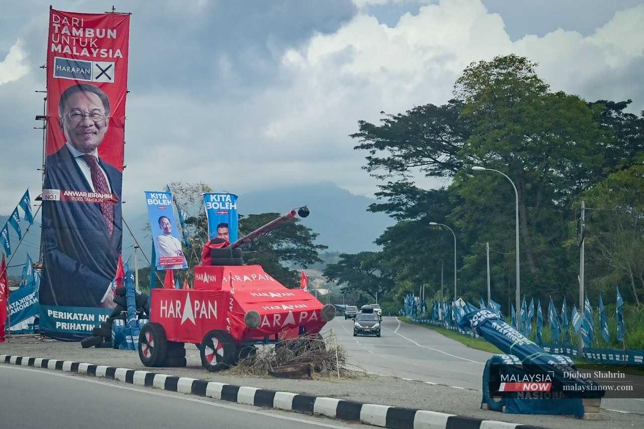 A giant poster of Pakatan Harapan chairman Anwar Ibrahim towers over a replica tank and cannon covered in PH and Perikatan Nasional flags at a junction in Tambun, Perak.