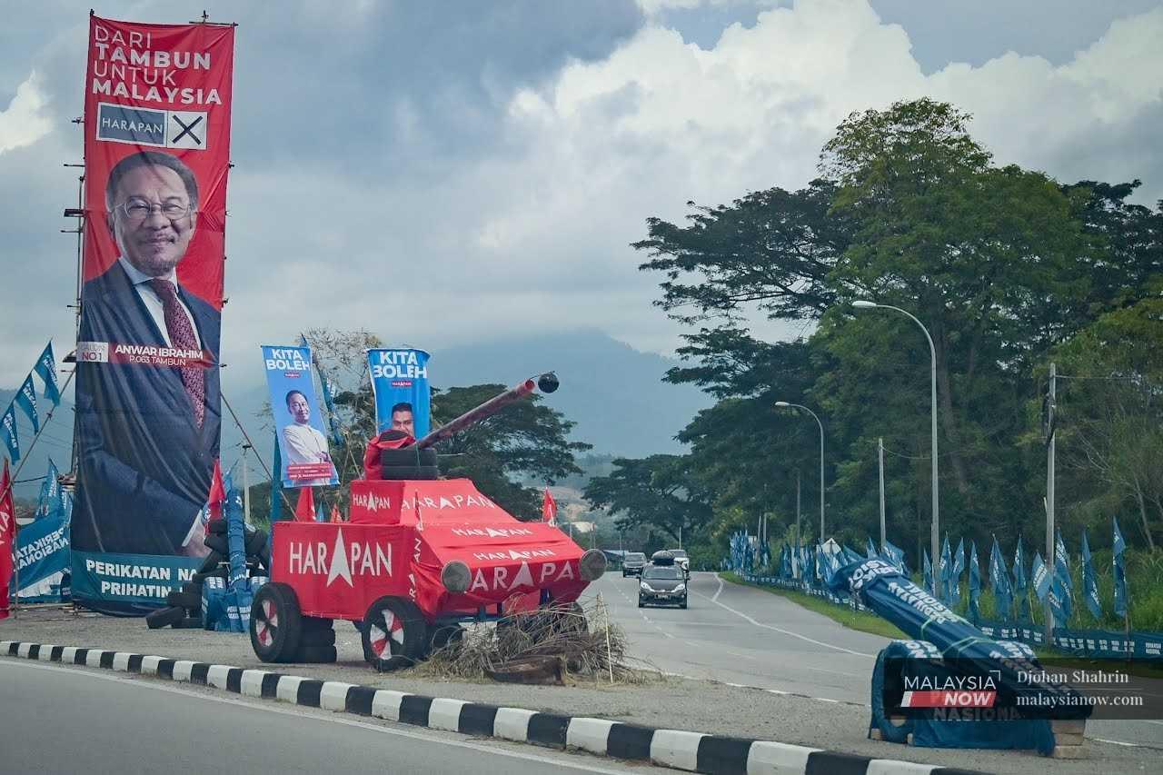 Poster gergasi Pengerusi Pakatan Harapan Anwar Ibrahim dan replika kereta kebal diletakkan di hadapan meriam berbalut bendera Perikatan Nasional di sebuah jalan raya di Tambun, Perak.