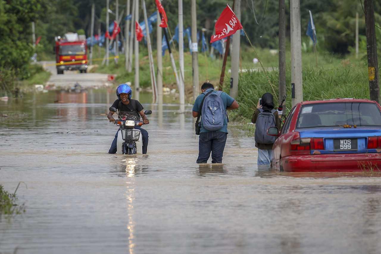 People and vehicles make their way through a flooded road in Kampung Sri Tanjung, Dengkil, Nov 17. Photo: Bernama