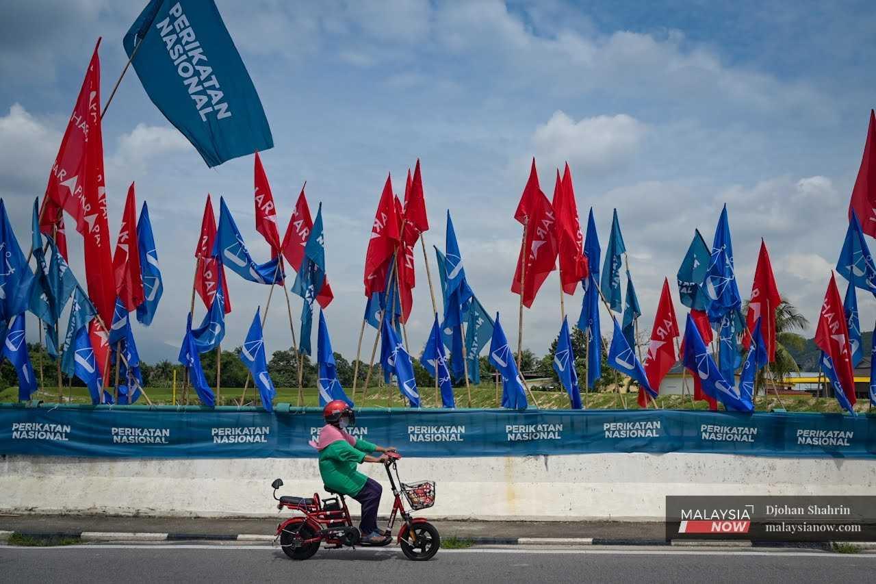 A woman rides an e-scooter past a row of party flags at the Kampung Manjoi enclave in Tambun, Perak.
