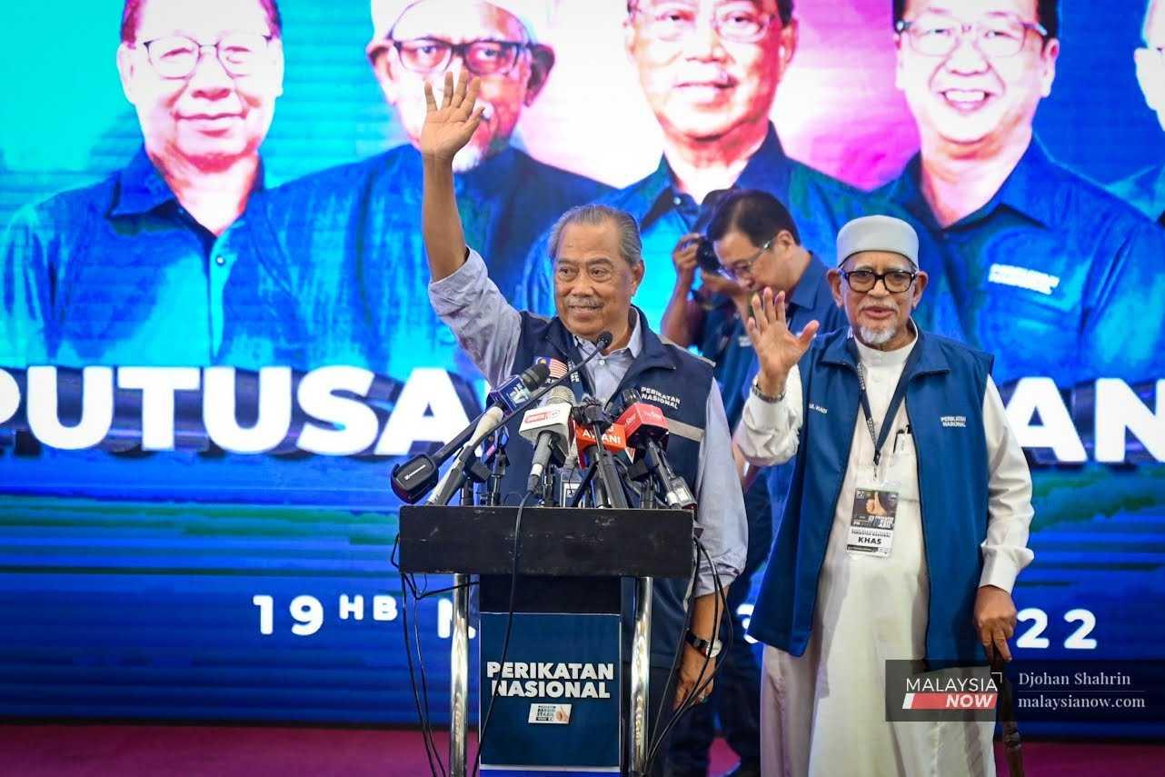 Presiden PAS Abdul Hadi Awang melambaikan tangan bersama Pengerusi Perikatan Nasional Muhyiddin Yassin selepas keputusan pilihan raya umum diumumkan di Shah Alam pada 20 November.