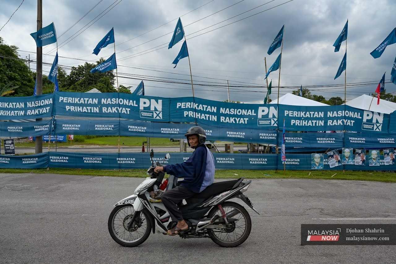 A motorcyclist passes a road decked out in Perikatan Nasional flags and banners in Tambun, Perak.