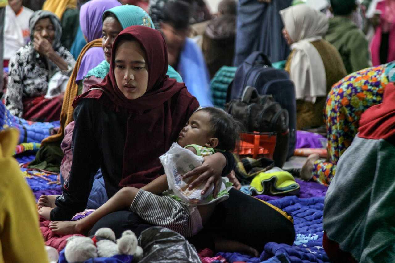 A woman holds a child as they shelter at a district office after being evacuated following the eruption of Mount Semeru in Lumajang, East Java province, Indonesia, Dec 4, in this photo taken by Antara Foto. Photo: Reuters