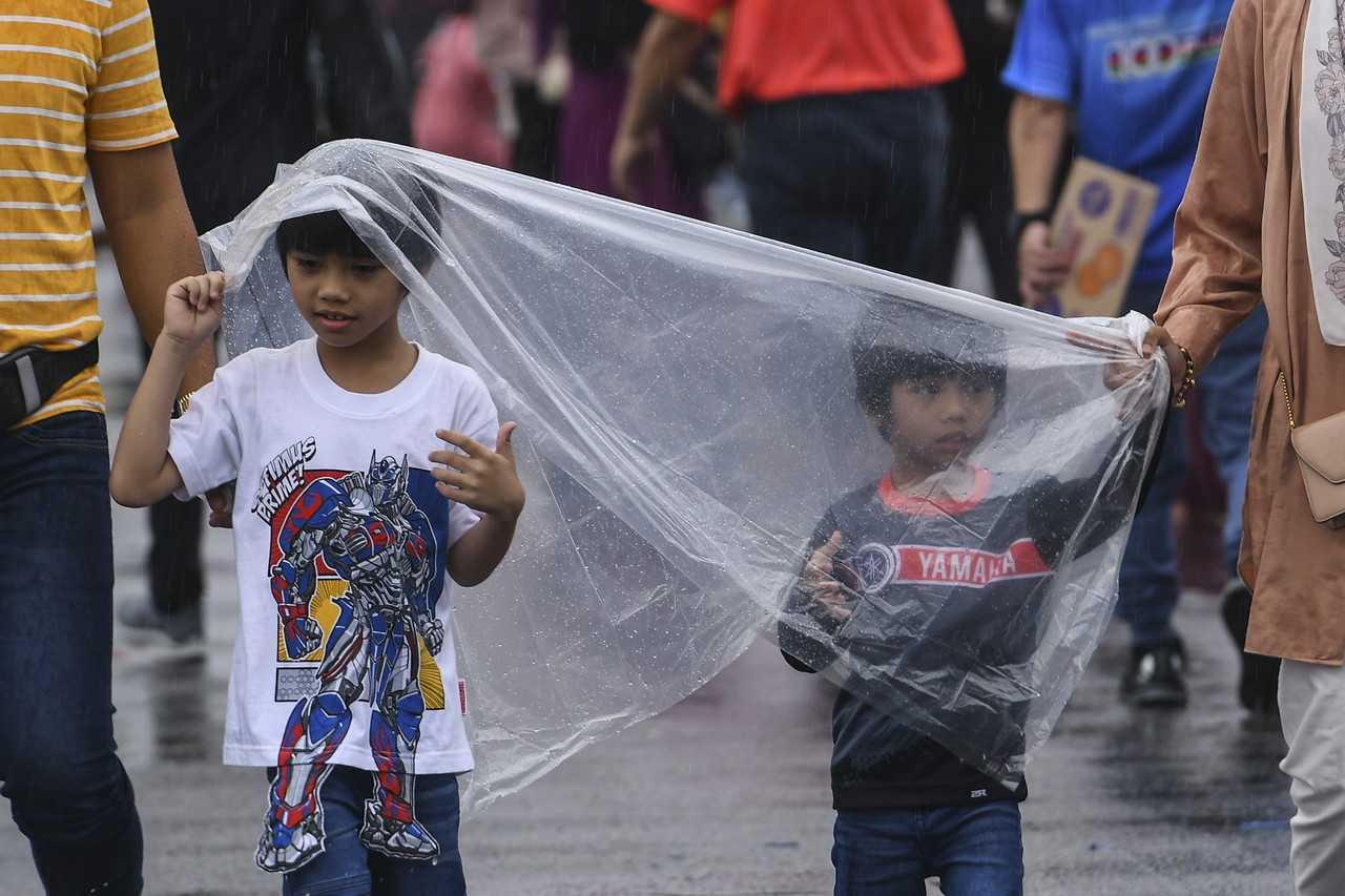 Children use a plastic sheet to shield themselves from the rain at Pasar Manir in Kuala Terengganu. Photo: Bernama