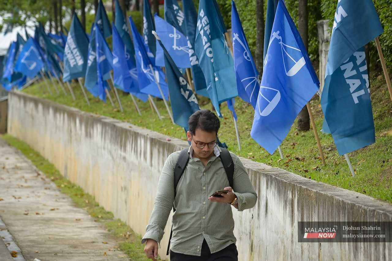 A man looks at his phone as he passes a row of Perikatan Nasional and Barisan Nasional flags in Tasik Permaisuri, Cheras, in Kuala Lumpur, ahead of the 15th general election. 
