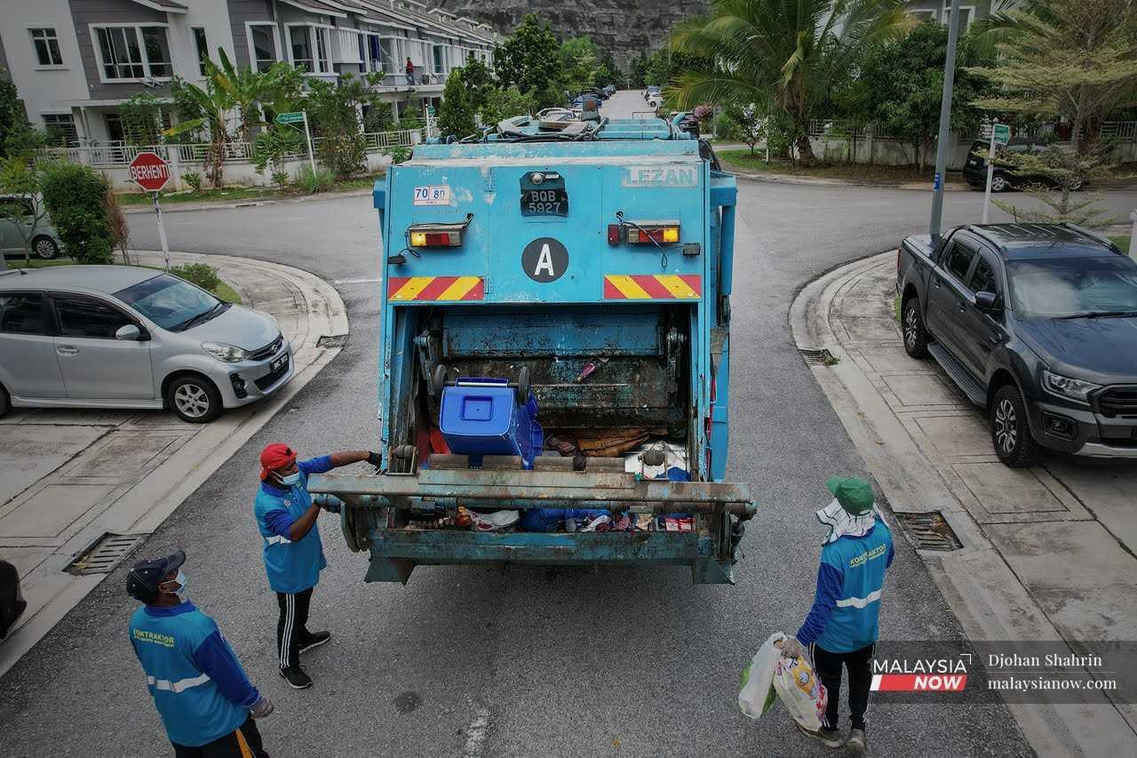 Rizal drives the garbage truck around a housing area in Bukit Bandaraya, Shah Alam, while his colleagues collect the bags of rubbish and throw them into the back.