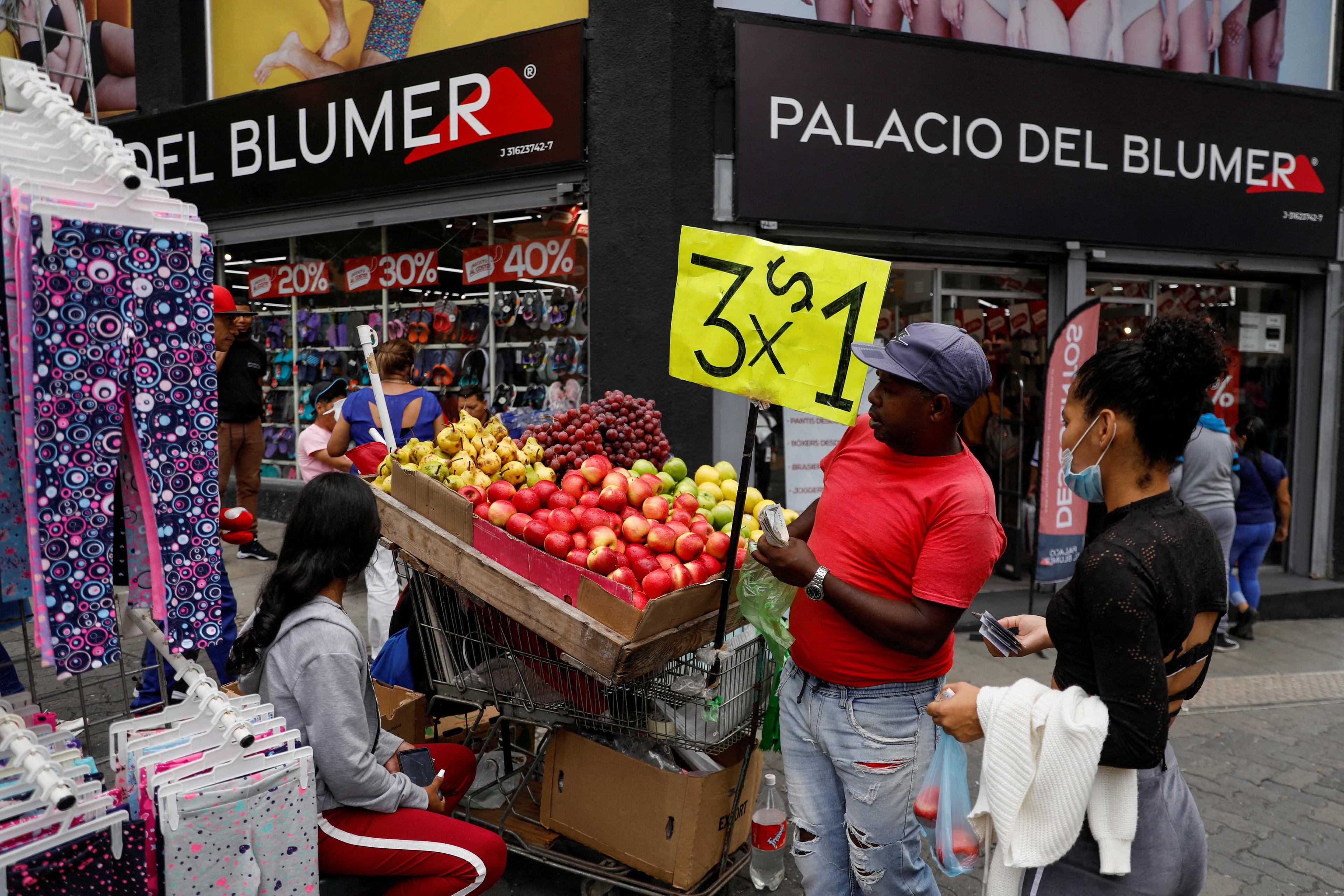 A woman buys apples at a street stand with a sign reading '3 for US$1,' in Caracas, Venezuela Aug 25. Photo: Reuters