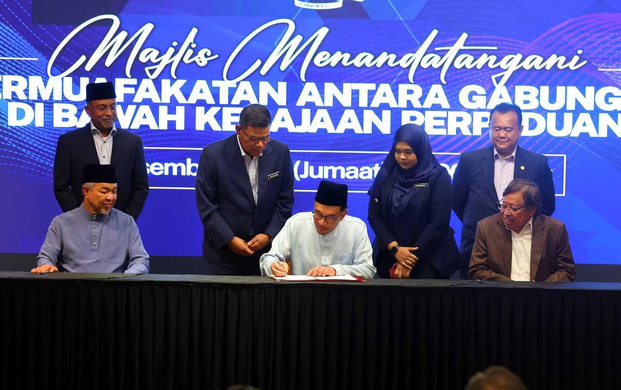 Perdana Menteri Anwar Ibrahim (tengah) menandatangani perjanjian persefahaman bersama ketua parti lain termasuk Pengerusi Barisan Nasional Ahmad Zahid Hamidi (kiri) dan Pengerusi Gabungan Parti Sarawak Abang Johari Openg (kanan) di Putrajaya pada 16 Disember. Gambar: Bernama