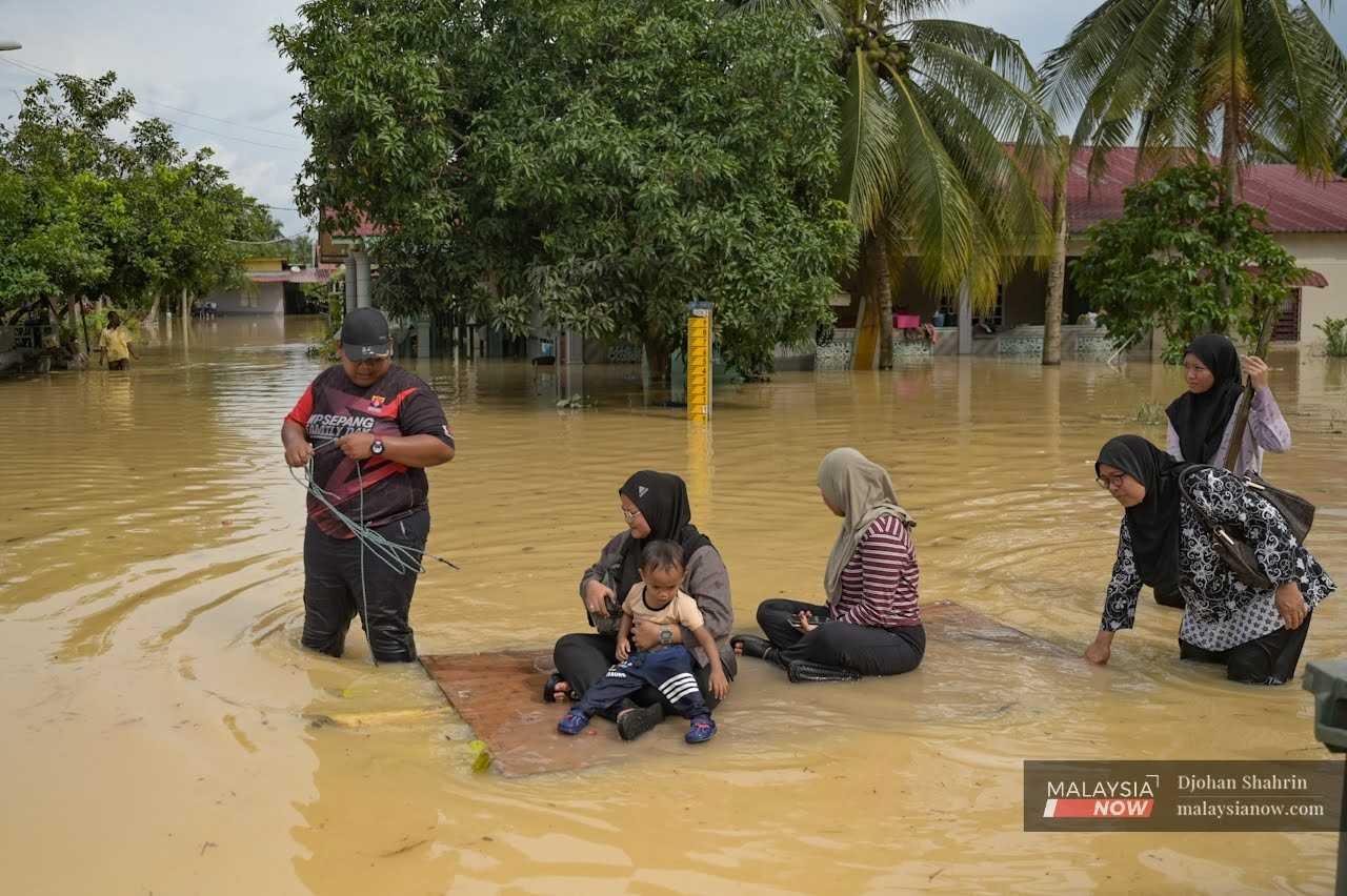 Seorang penduduk kampung menarik papan sebagai rakit untuk membawa keluarganya meredah banjir di Kampung Sungai Melut, Dengkil pada 18 November.