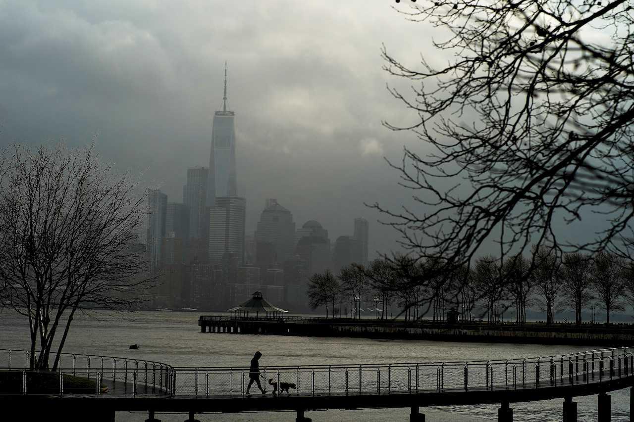 A woman walks her dog in a local park in Hoboken, New Jersey, while storm clouds pass by the One World Trade Center in New York, Dec 23. Photo: Reuters