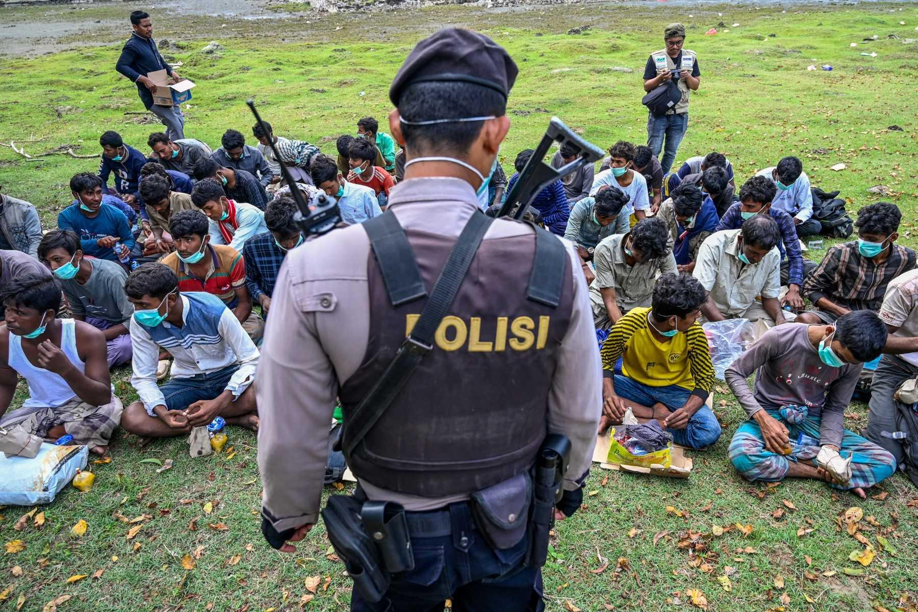 A policeman stands guard next to a group of Rohingya refugees waiting to be transferred to a temporary shelter following their arrival by boat in Krueng Raya, Indonesia's Aceh province, Dec 25. Photo: AFP