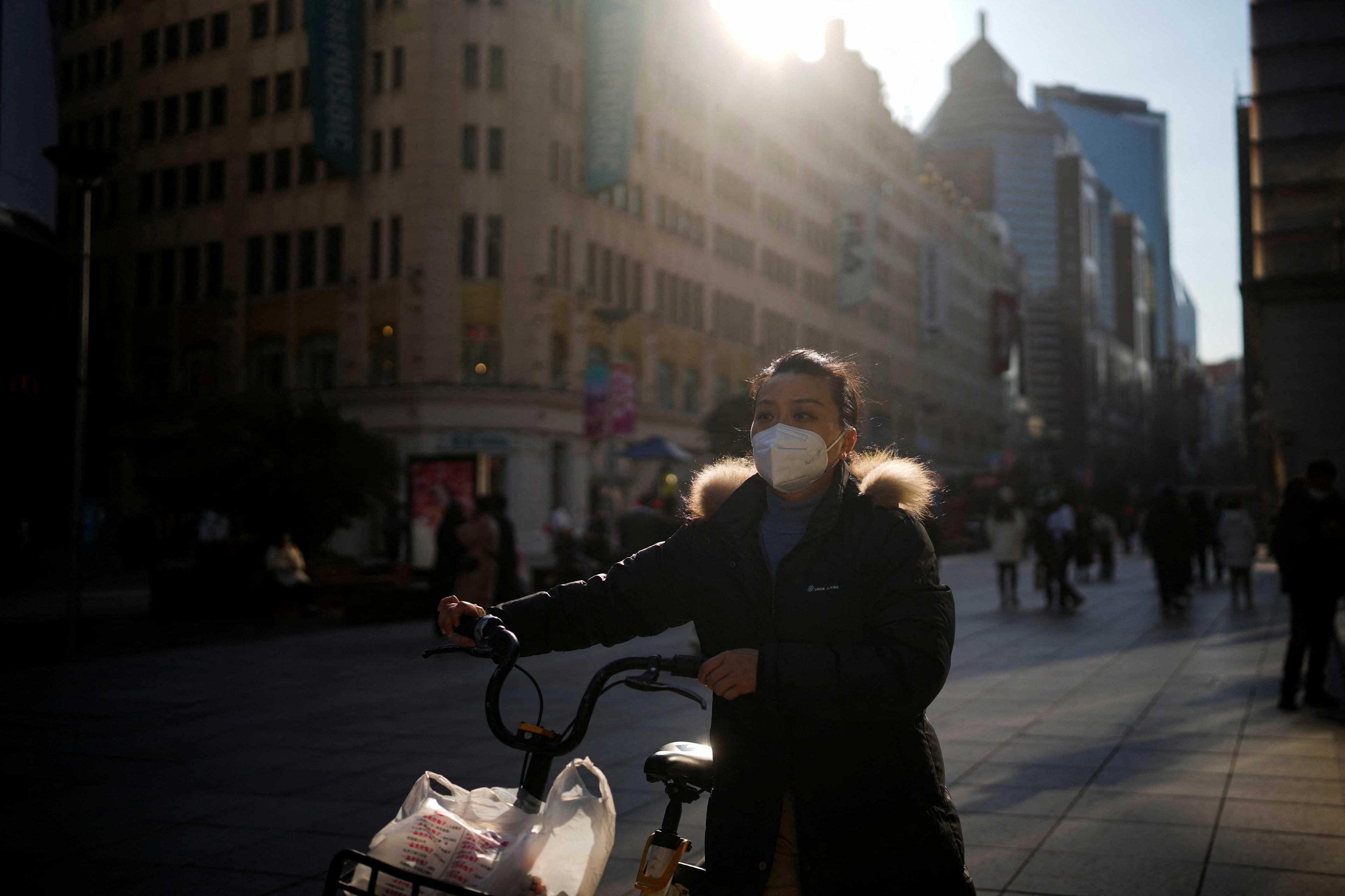 A woman wearing a protective mask walks with a bicycle in a shopping district as China returns to work despite continuing Covid-19 outbreaks in Shanghai, China, Jan 3. Photo: Reuters