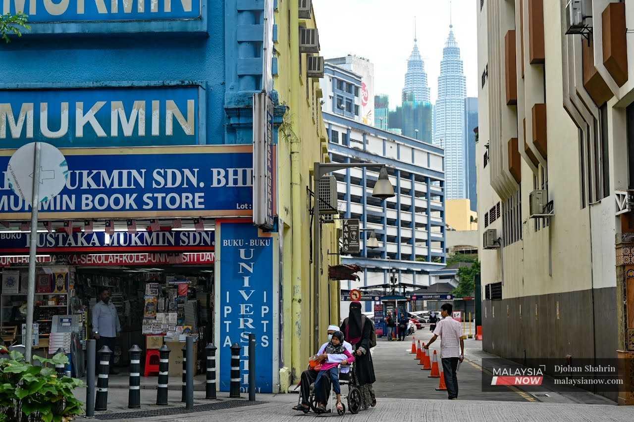 Seorang wanita menolak suami yang memakai pelitup muka dan anaknya menggunakan kerusi roda semasa berjalan di Jalan Tuanku Abdul Rahman, Kuala Lumpur.
