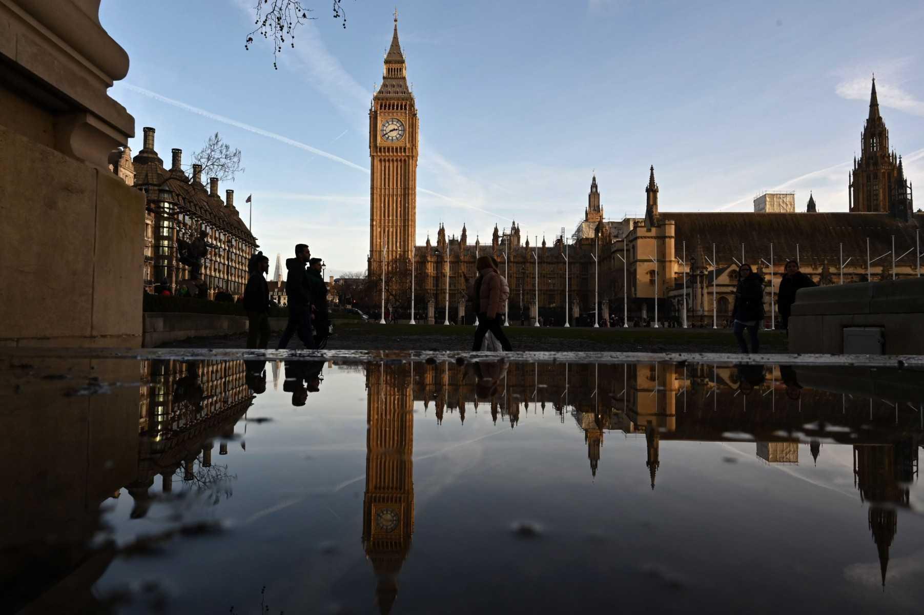 Pedestrians are reflected in a puddle of rain water opposite the Elizabeth Tower and the Palace of Westminster, home to the Houses of Parliament, in central London on Jan 4. Photo: AFP 