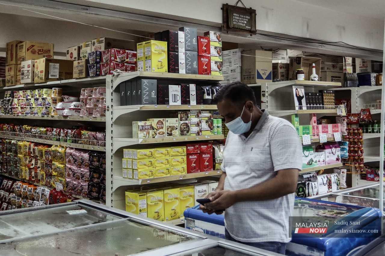 Pekerja asing sedang memeriksa bekalan menggunakan telefon pintar di sebuah kedai di Kajang.