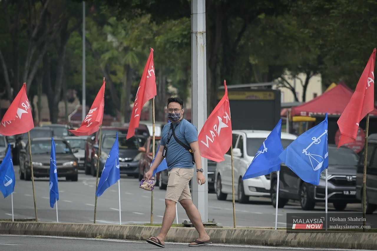 A pedestrian checks for traffic as he crosses a road in Tasik Permaisuri, Cheras, decorated with Pakatan Harapan and Barisan Nasional flags, ahead of last year's general election, Nov 3, 2022.
