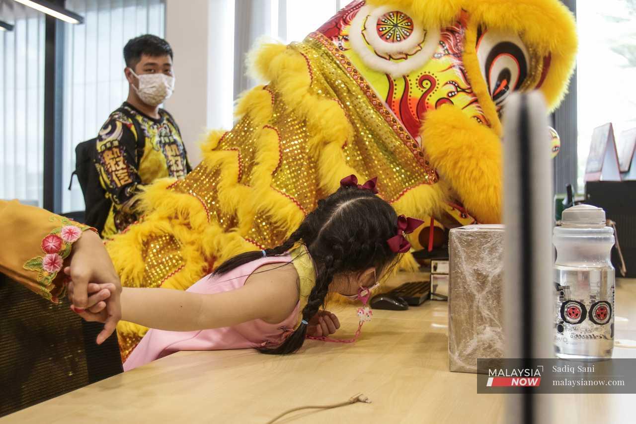 A young girl leans over to peer at the dancers under the lion's costume. 