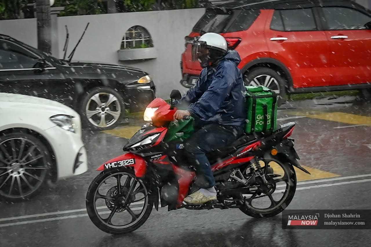 Penghantar makanan dalam talian meredah hujan lebat ketika menghantar pesanan kepada pelanggan di Taman Nirwana, Ampang, 9 Disember 2022.