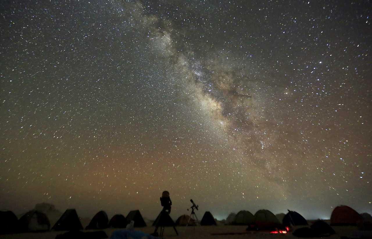 The Milky Way is seen in the night sky around telescopes and camps of people over rocks in the White Desert north of the Farafra Oasis southwest of Cairo, May 16, 2015. Photo: Reuters