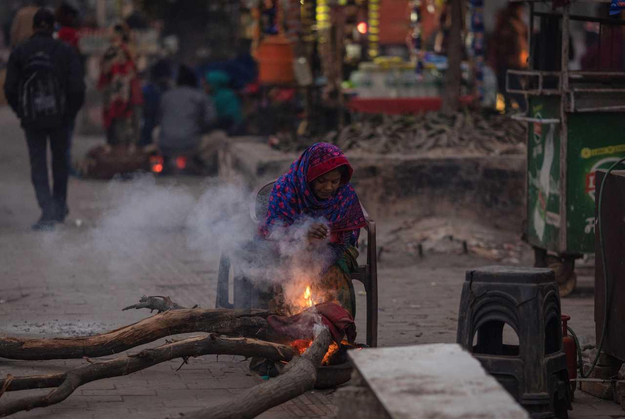 A woman sits beside a bonfire next to her tea stall at a roadside during a cold winter morning in New Delhi, India. Photo: Reuters
