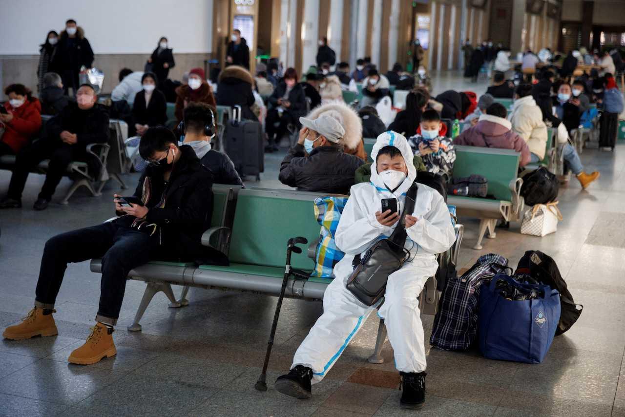 A person wearing a protective suit sits at the Beijing Railway Station as passengers wait to board a train ahead of the Lunar New Year festivities in Beijing, Jan 20. Photo: Reuters