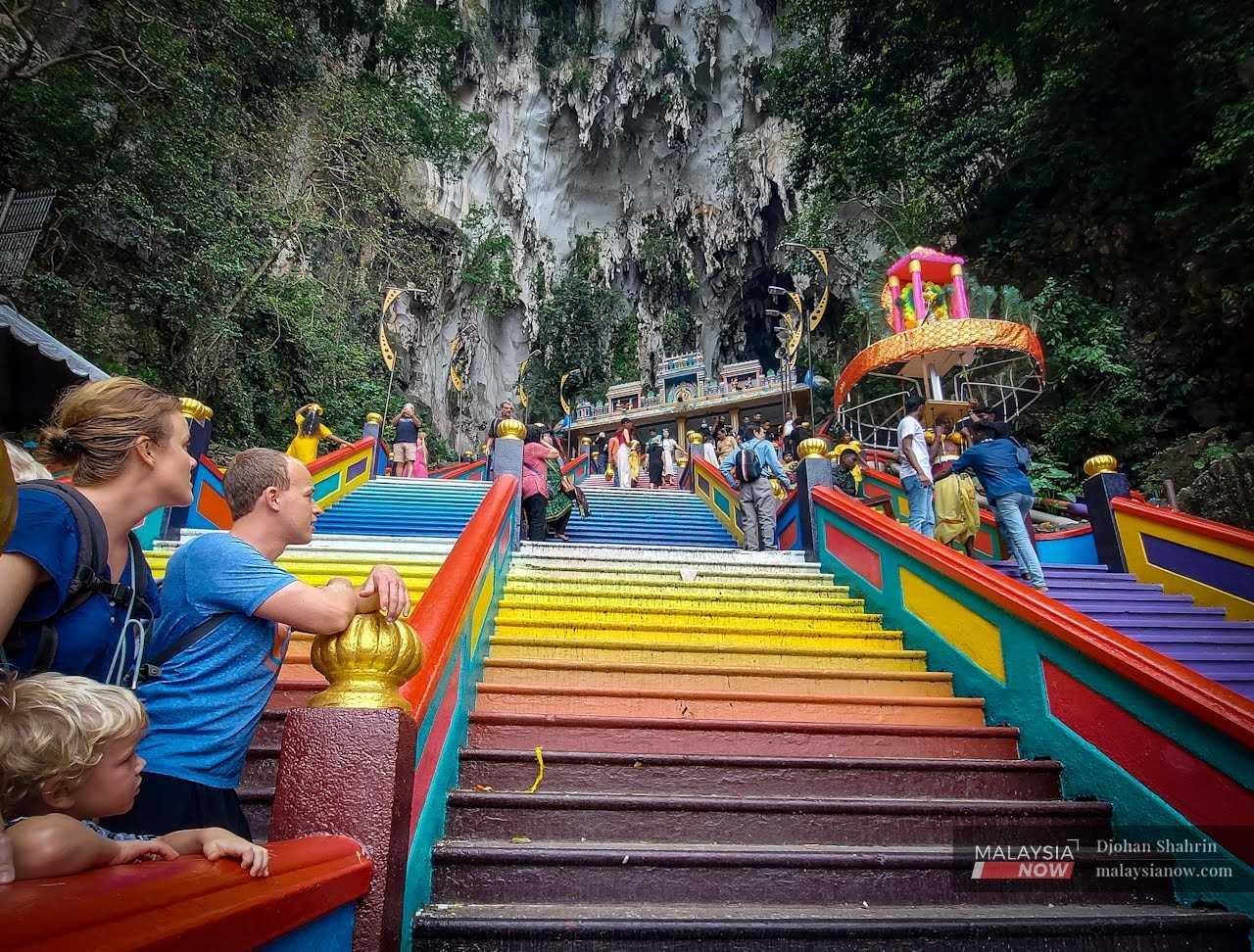 Tourists watch as Hindu devotees carry a kavadi up the steps at the Batu Caves temple.  
