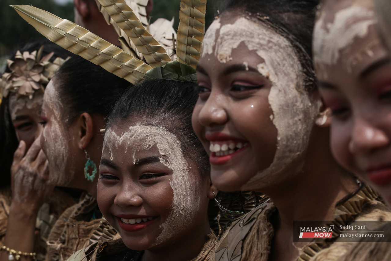 Mah Meri girls wearing traditional outfits and headgear smile, enjoying the sights and sounds of the day. 