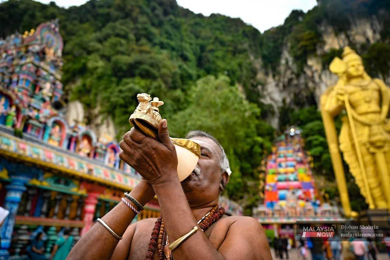 A man blows a traditional horn in a call to the devotees at Batu Caves. 
