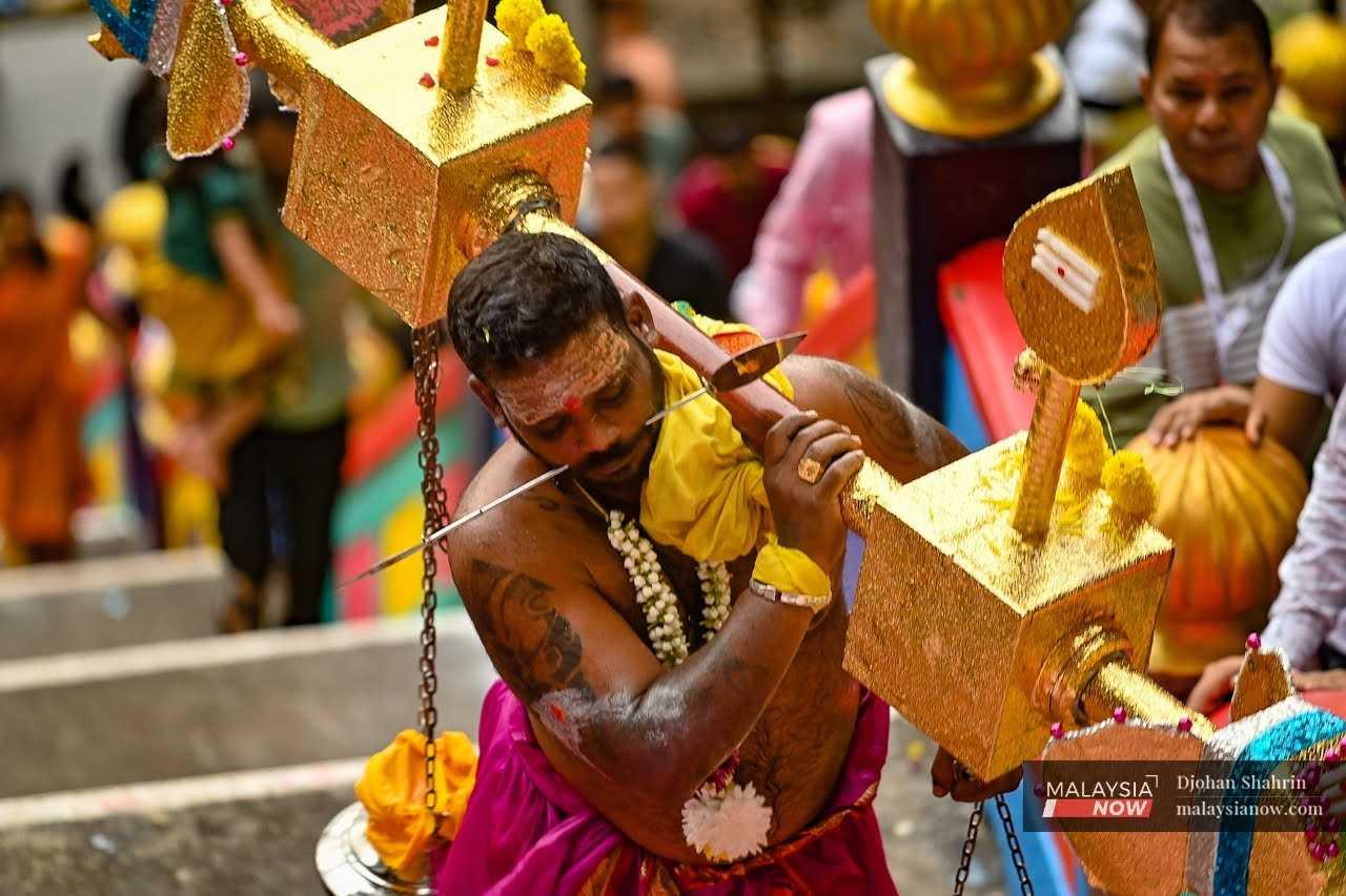 A man with piercings through his cheeks carries a golden kavadi up the steps. 