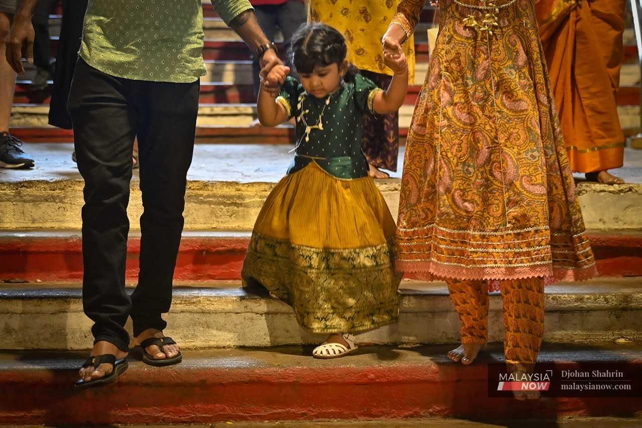 A young girl clings to her parents' hands at the temple. 
