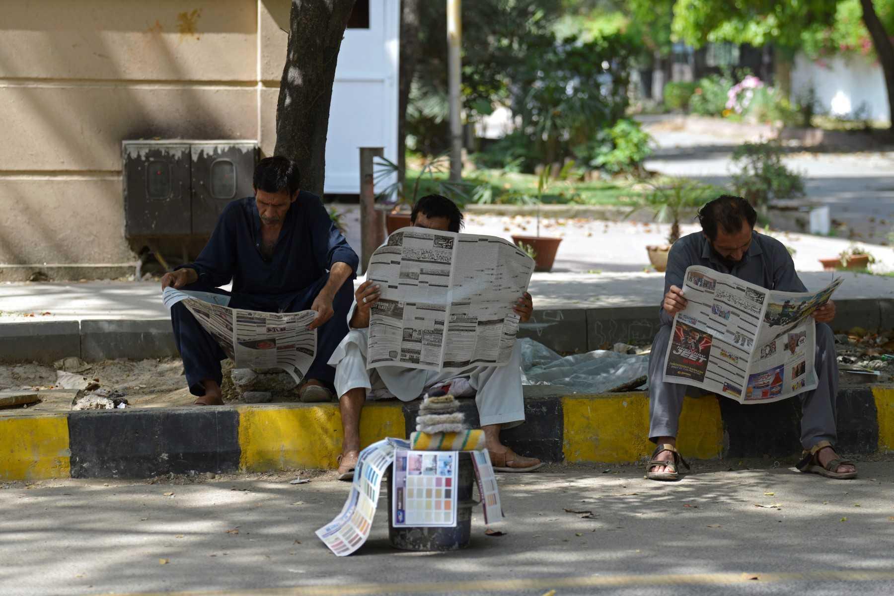 Residents read newspapers along the roadside in Islamabad, Pakistan, on April 10, 2022. Photo: AFP