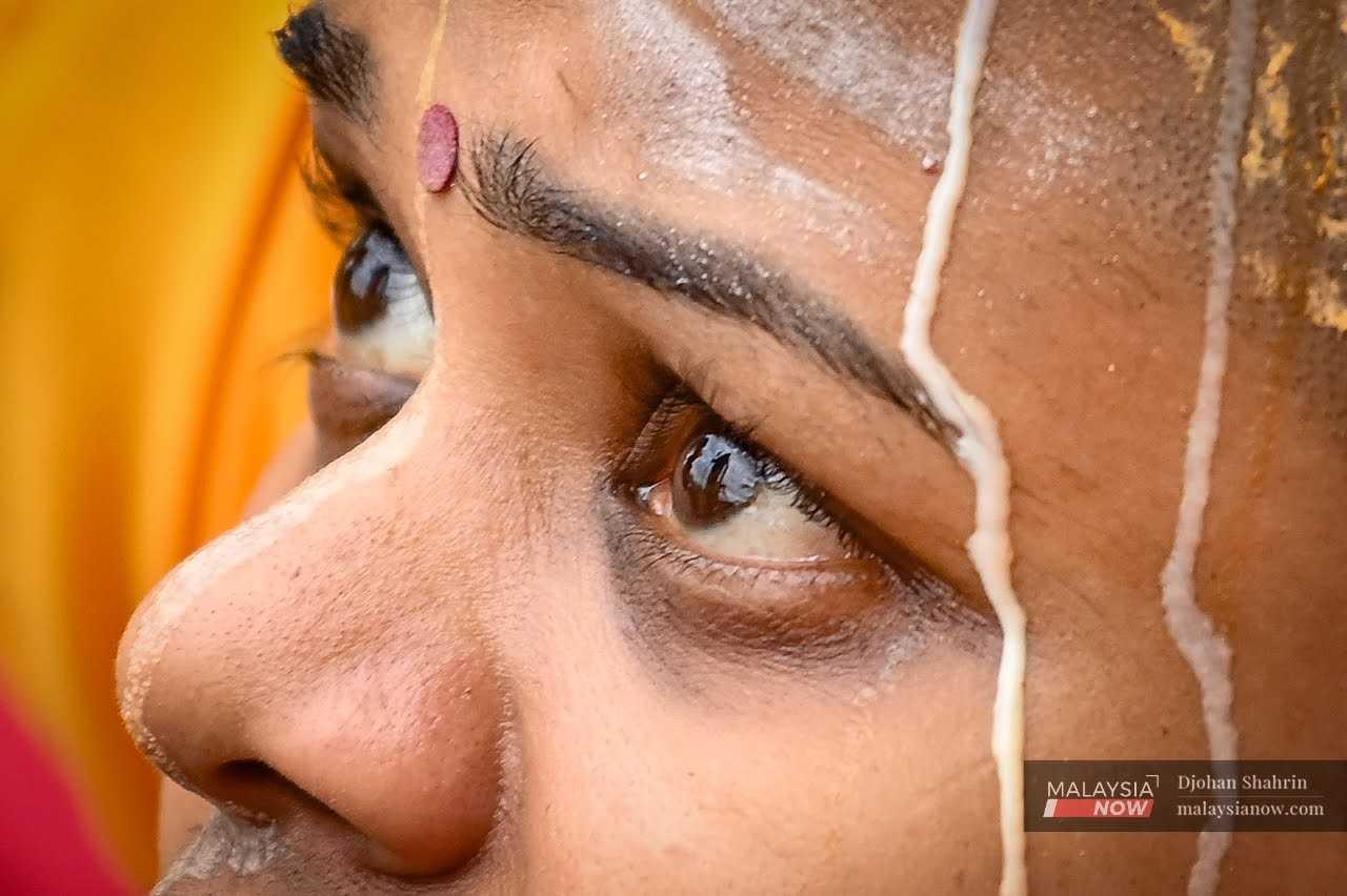 Milk trickles down a woman's face as she looks up at the golden statue of Lord Murugan at the Batu Caves temple.