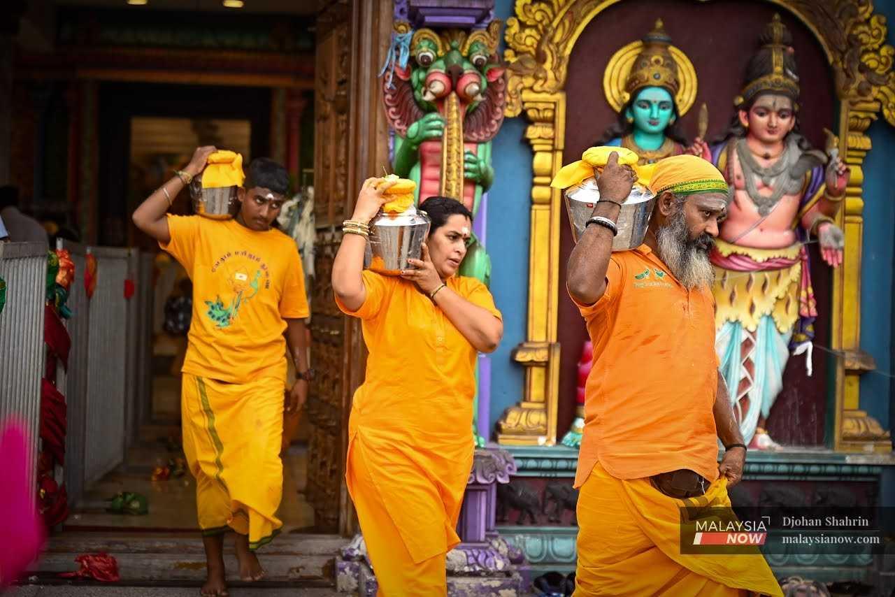 Penganut Hindu berpakaian kuning membawa bekas berisi susu di bahu mereka.