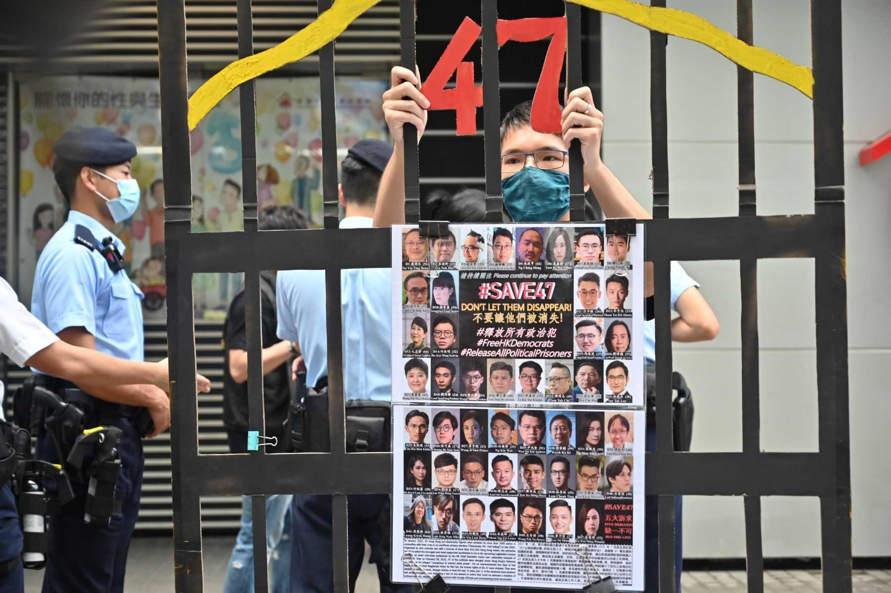 In this file photo taken on Sept 19, 2021 a protester in Hong Kong stands behind a mock jail with photos of the 47 pro-democracy figures currently in prison. Photo: AFP