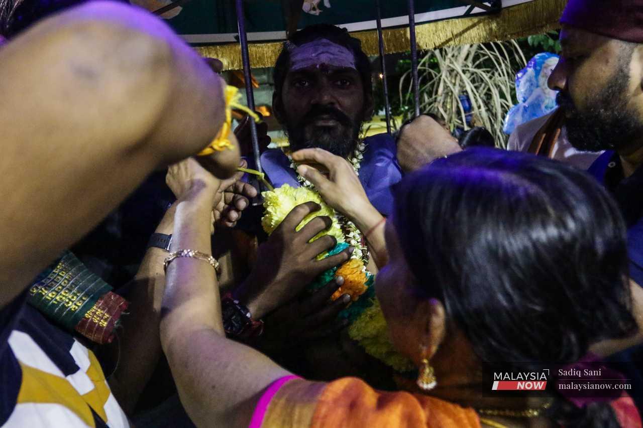 His mother puts a garland of flowers around his neck as his friends help position the kavadi on his shoulders. 
