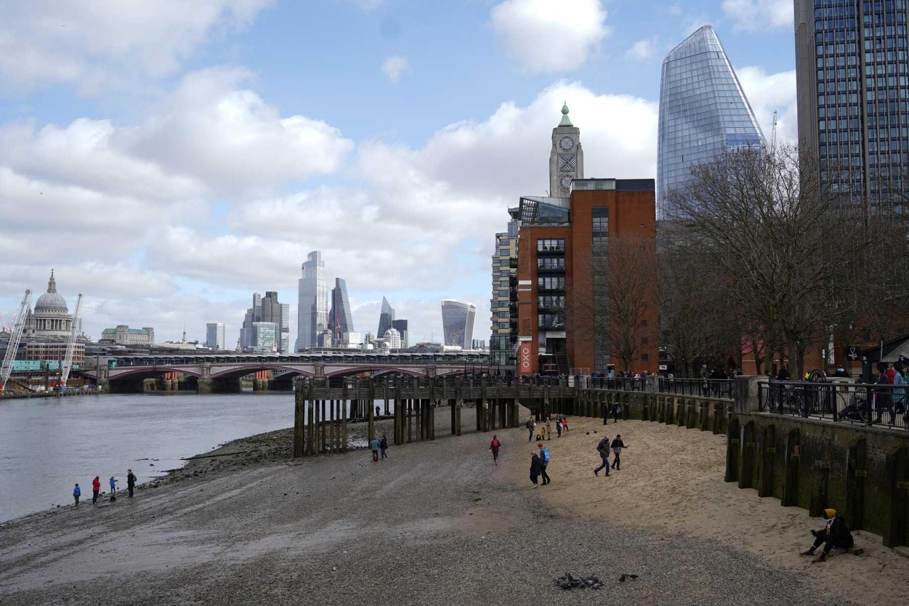 People take their daily exercise at low tide beside the River Thames on the South Bank in London on March 21, 2021. Photo: AFP