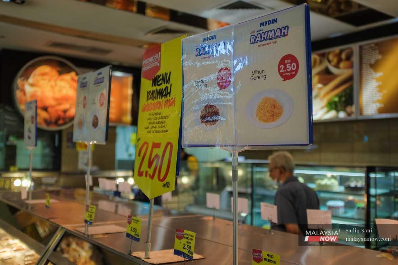 Seorang pekerja berjalan di belakang kaunter kedai makan yang menyediakan hidangan Menu Rahmah di sebuah pasar raya di Subang, Selangor.