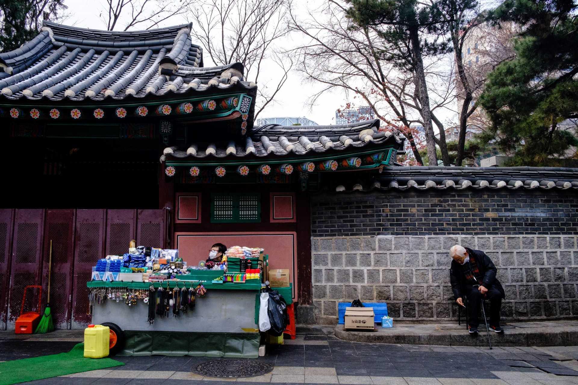 A street vendor minds her stall as a man sitting nearby flicks ash from his a cigarette in Seoul on Jan 5. Photo: AFP