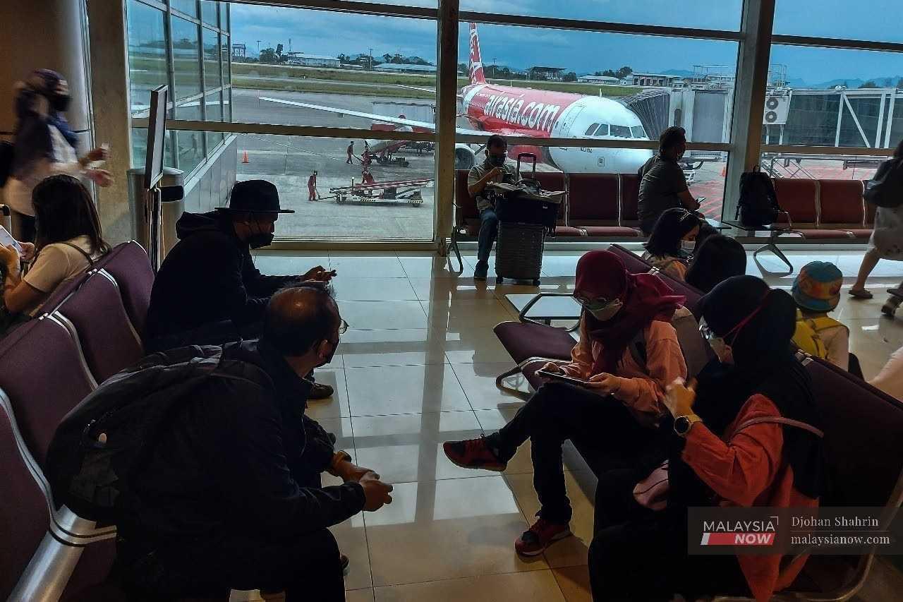 Passengers wait outside their boarding gate as an AirAsia plane sits on the tarmac at the Kuching International Airport. 
