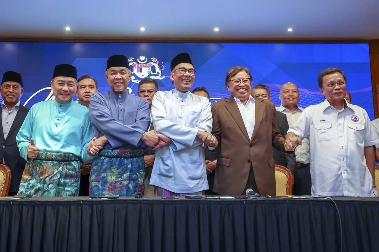 Prime Minister Anwar Ibrahim (centre) links arms with party leaders at the signing of a memorandum of understanding in Putrajaya on Dec 16. Photo: Bernama