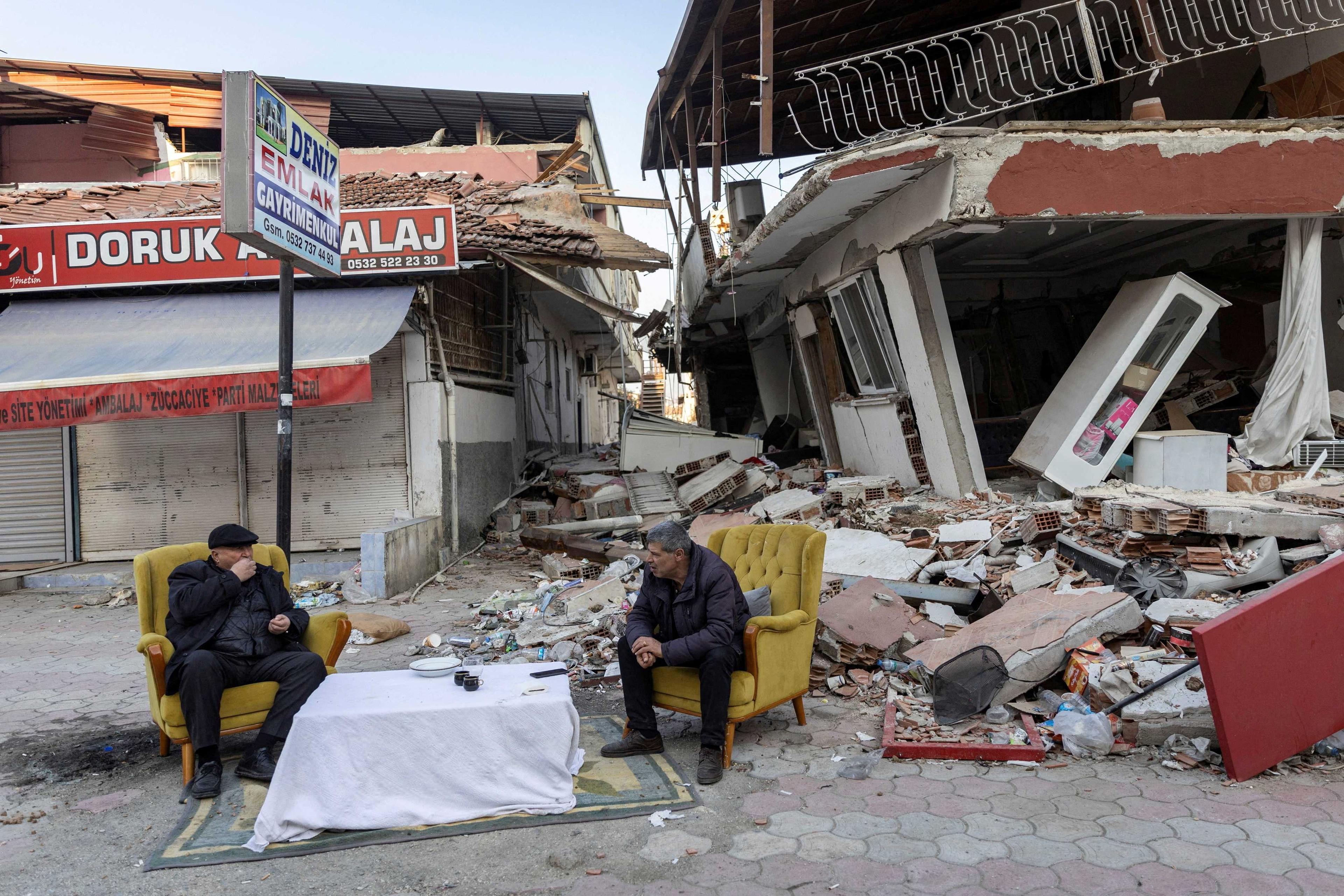 Dua lelaki sedang duduk dan bersembang di hadapan harta benda yang musnah selepas gempa bumi maut di wilayah Hatay, Turkiye, 20 Februari. Gambar: Reuters